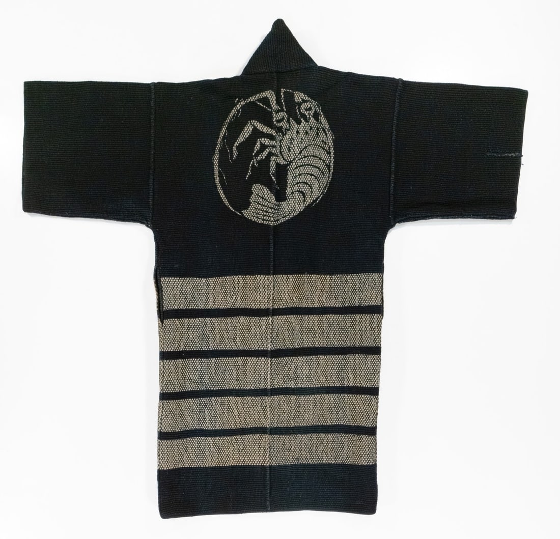 A REVERSIBLE JAPANESE FIREMAN'S COAT, ADAIR ESTATE: One design displays a crest depicting an auspicious ebi above horizontal bands while the interior displays a different dye resist design of a repeating geometric floral pattern. The inscription on the