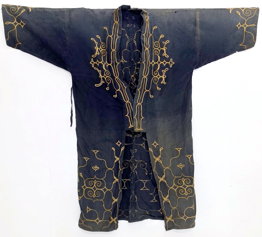 A JAPANESE AINU CEREMONIAL ROBE WITH APPLIQUE: The dark indigo cloth robe decorated with traditional appliqued and embroidered Ainu motifs surrounding the neck opening, sleeves, and lower body originates with the Indigenous Ainu people of northern
