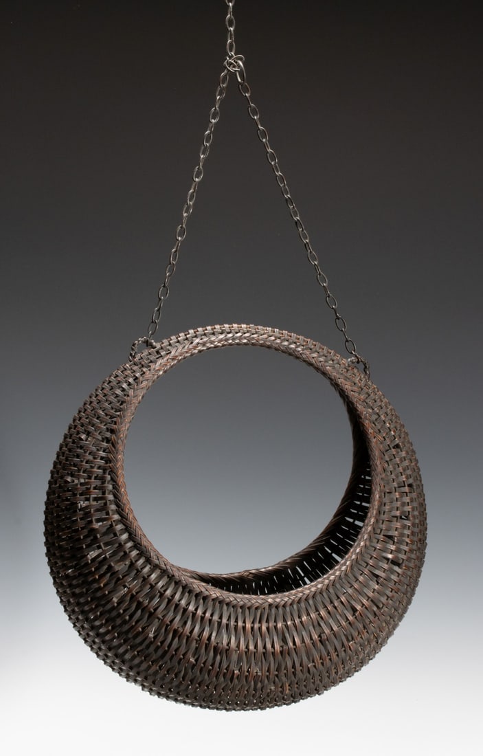 A 'FULL MOON' JAPANESE BAMBOO BASKET, ADAIR ESTATE: The moon form basket for flower arranging is woven with a tightly plaited rim that defines a circular open perimeter like a full moon. The body is woven as a trough for flowers, the rounded top is met