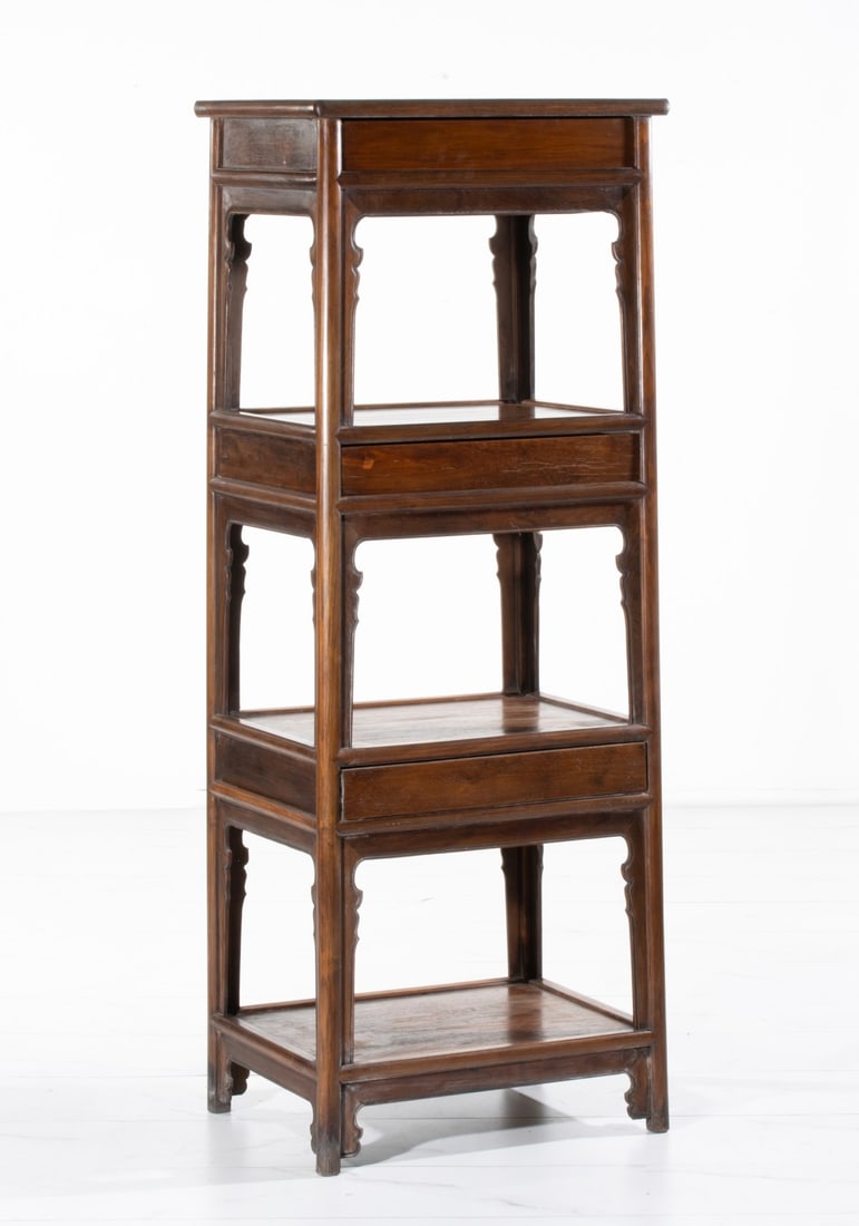 A CHINESE CARVED HUANGHALI TYPE HARDWOOD ETAGERE: The three-tier etagere featuring mortise-and-tenon construction and three hidden drawers. Measures 65H x 24W x 18.5D inches. Provenance: The estate of John Adair Jr. (1942-2025), founder and proprieto