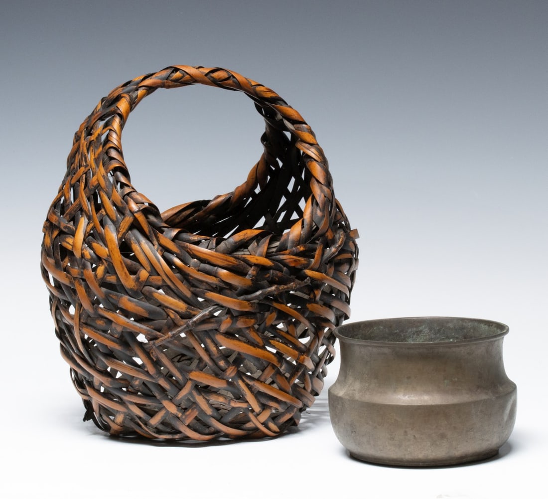 A RUSTIC JAPANESE BAMBOO IKEBANA BASKET ADAIR ESTATE: The rough weave basket with integrated handle that emerges seamlessly from the body is accented by a natural bamboo stalk and is accompanied by its original liner. Measures 10.5 x 9 x 7.5 inches. Prov