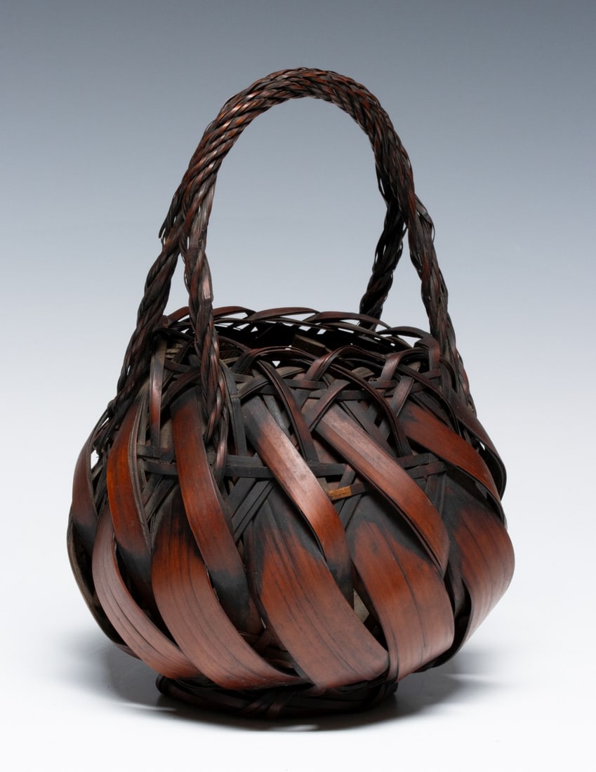 WIDE SPLINT ROPE TWIST JAPANESE HANAKAGO, ADAIR ESTATE: The wrapped and woven body in rich smoked colors incorporates a high arching braided handle, good patina, unsigned. Measures 9.5 6.5 x 6.5 inches. Provenance: The estate of John Adair Jr. (1942-2025),
