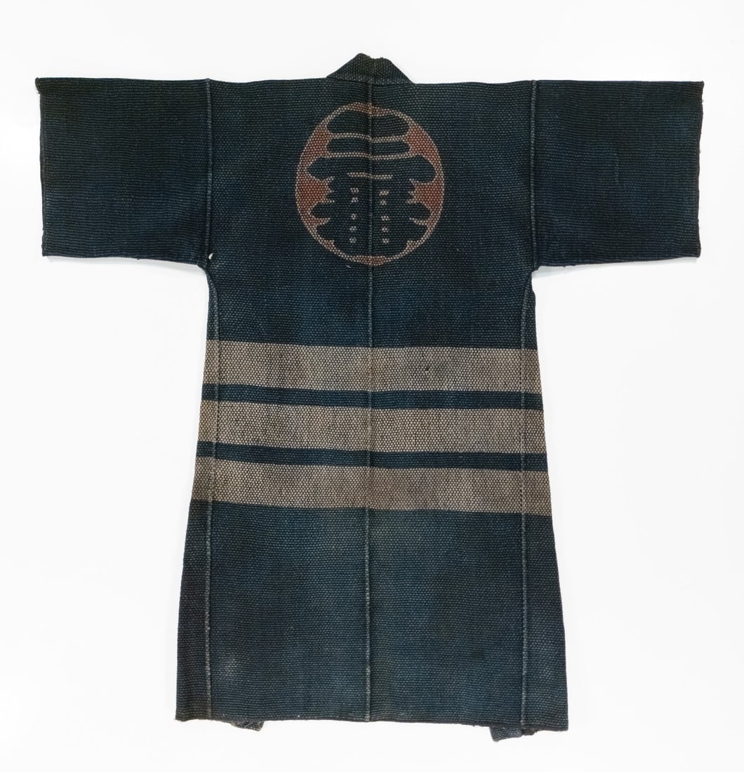 A JAPANESE FIREMAN'S COAT WITH CREST, ADAIR ESTATE: The back displays a large circular firefighting brigade, sponsor organization or merchant's emblem above horizontal bands. Additional inscriptions on the lapels may refer to a merchant association. Th