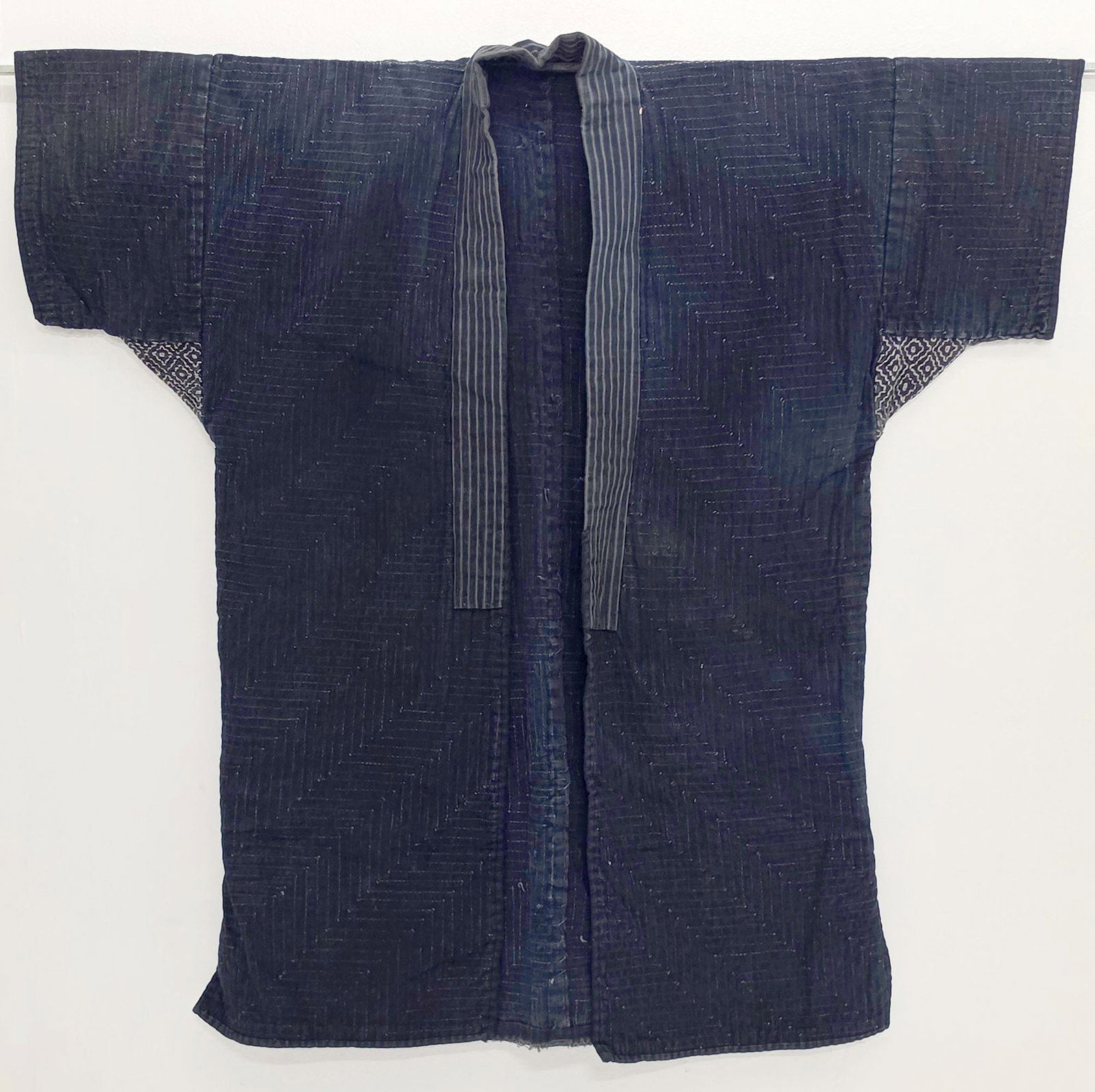 A LATE 19TH TO EARLY 20TH CENTURY JAPANESE WORK JACKET: The traditional indigo dyed garment is quilted with sashiko stitch overall, and persimmon flower sashiko embroidery at the arms. Measures 35 x 35 inches. Provenance: The estate of John Adair Jr. (1942