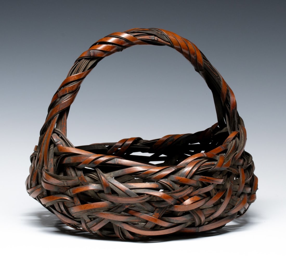 A NEST FORM JAPANESE BAMBOO FLOWER BASKET, ADAIR ESTATE: The low, nest form basket with handle is woven to create a dynamic and disorderly character in rustic overtones. Measures 11 x 13 x 12 inches. Provenance: The estate of John Adair Jr. (1942-2025), fou
