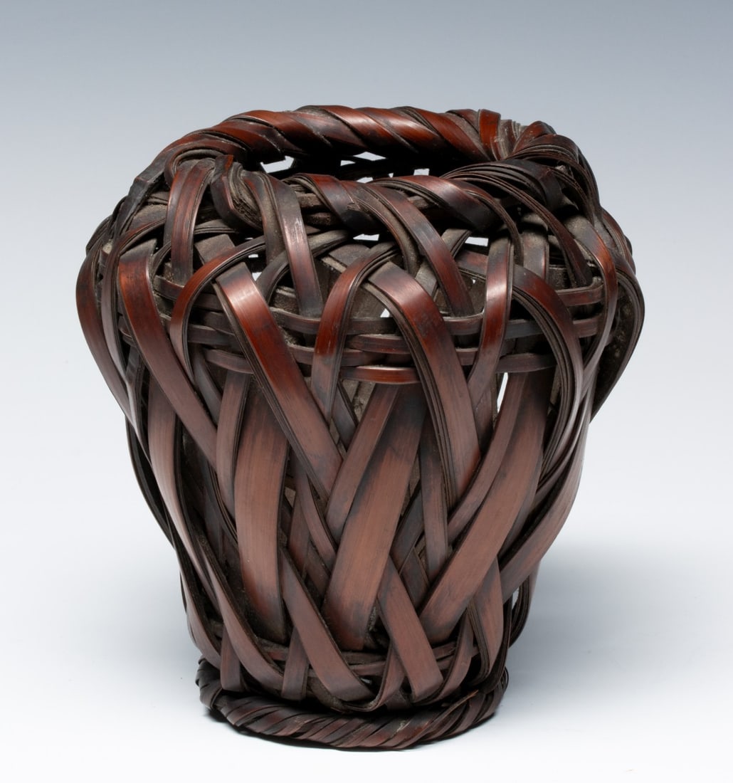 A VASIFORM JAPANESE BAMBOO IKEBANA BASKET, ADAIR ESTATE: The high-shouldered tapering form on a robust, corded pedestal foot is composed of wide, thick bamboo interlaced in a vigorous weave that creates a muscular, construction. The rim is finished with a