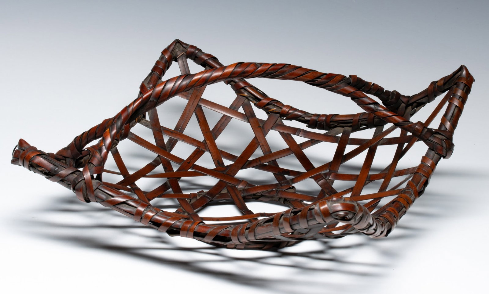 A DISHED SQUARE JAPANESE IKEBANA BASKET, ADAIR ESTATE: The shallow, flared square form of woven bamboo in fine patina sits on an integrated circular foot-ring. Measures 6 x 13 x 13 inches. Provenance: The estate of John Adair Jr. (1942-2025), founder and 