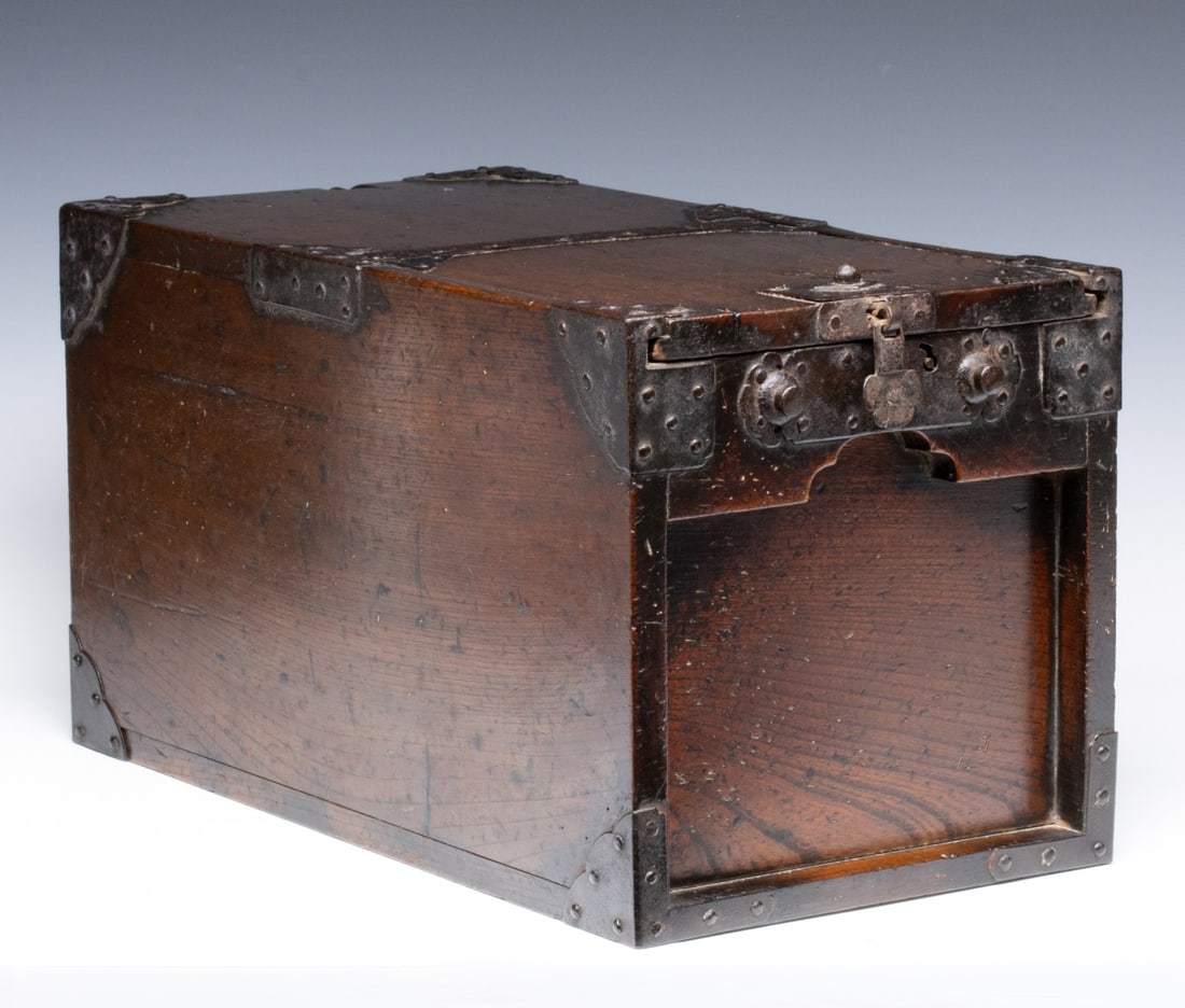 A MEIJI PERIOD KEYAKI WOOD MONEY BOX WITH IRON MOUNTS: The heavy, warmly patinated box has a lift top that opens to an interior compartment and small sliding drawer. Measures 10.75 x 10.5 x 19.5 inches. Provenance: The estate of John Adair Jr. (1942-2025)