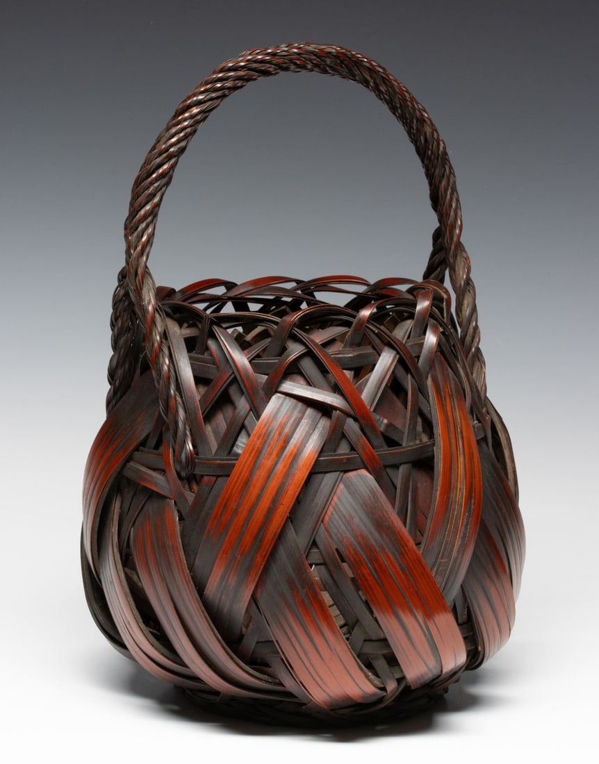 A JAPANESE BROAD SPLINT AND LACED BASKET, ADAIR ESTATE: The bold and expressive example is dominated by wide, curved bamboo splints interlocked within a complex random-weave below the rim with airy arching laces joining a thick, tightly twisted bamboo