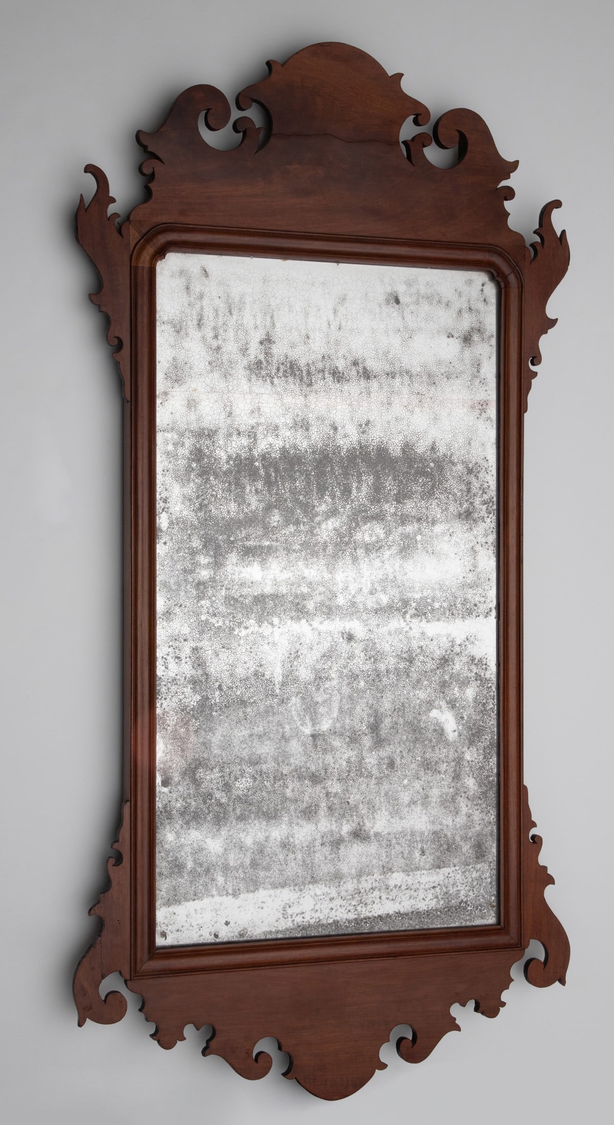 A JOHN ELLIOTT PHILADELPHIA CHIPPENDALE MIRROR C. 1760: The American Chippendale mahogany looking glass with elaborate scroll cut frame and the original mirror plate is found with the original John Elliott paper label verso. Measures 45.5 x 24 inches. Prov