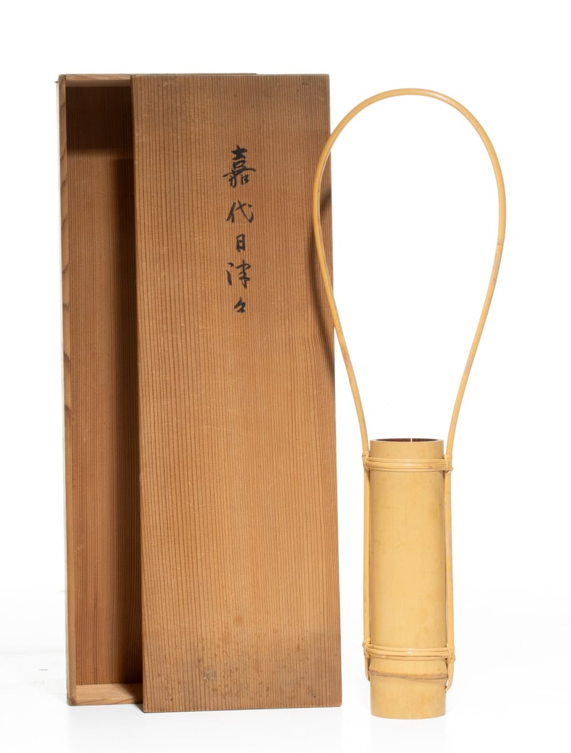 A JAPANESE BAMBOO FLOWER ARRANGING VASE, ADAIR ESTATE: The minimalist Japanese bamboo flower vessel formed from a smooth, natural section of a bamboo trunk with lower node is framed by an elegant, high arching overhead loop handle crafted from a single, s