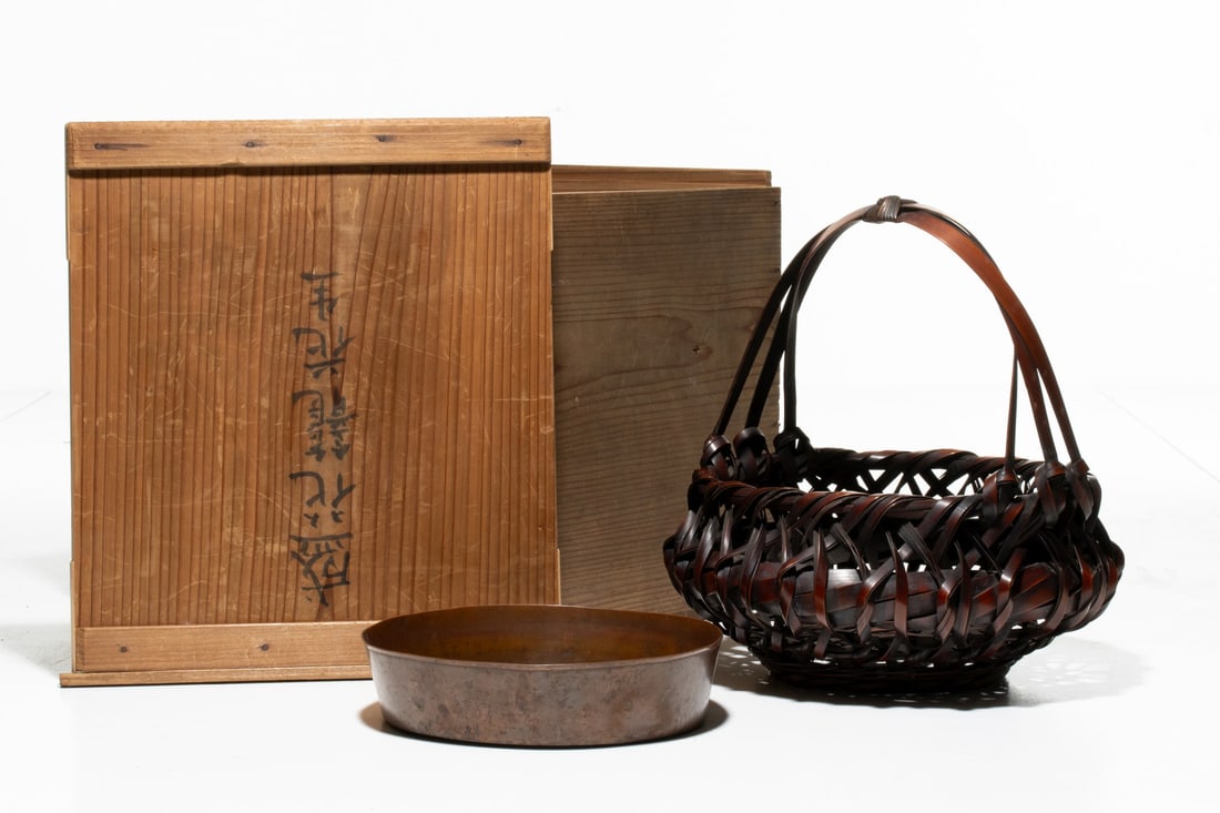 AN UNSIGNED JAPANESE BAMBOO BASKET W/LINER, ADAIR ES: The dark-lacquered Japanese bamboo flower basket features a wide, open-weave body formed from broad, split-bamboo. The basket has an arching multi-strand handle and original custom shallow copper basi