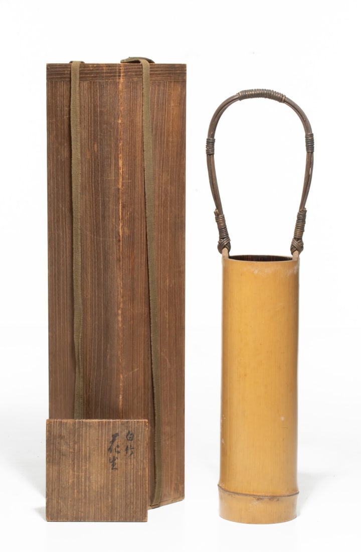 TANABE CHIKUUNSAI I BAMBOO FLOWER VESSEL, ADAIR ESTATE: The minimalist Japanese flower vessel is crafted from a single culm of natural honey-yellow bamboo joined by a handle made from bundled vine stalks bound tightly with fine dark rattan thread wrapping 