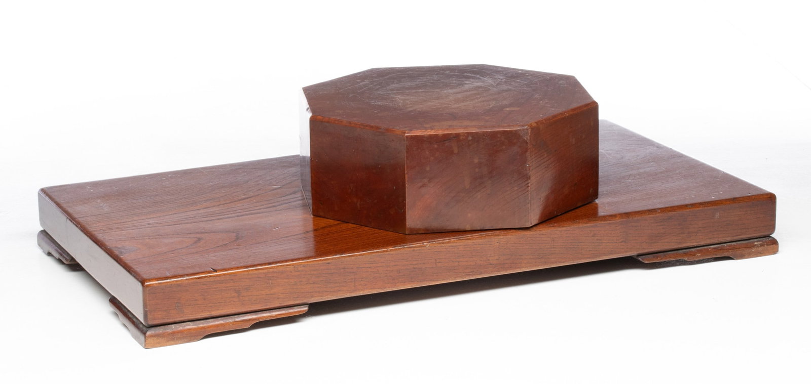 TWO SOLID KEYAKI WOOD TABLETOP STANDS: A solid eight-sided block and a thick slab on feet, both keyaki wood. Measures 3.75 x 9.75 x 9.75 and 2.25 x 22.75 x 12.5 inches. Provenance: The estate of John Adair Jr. (1942-2025), founder and prop