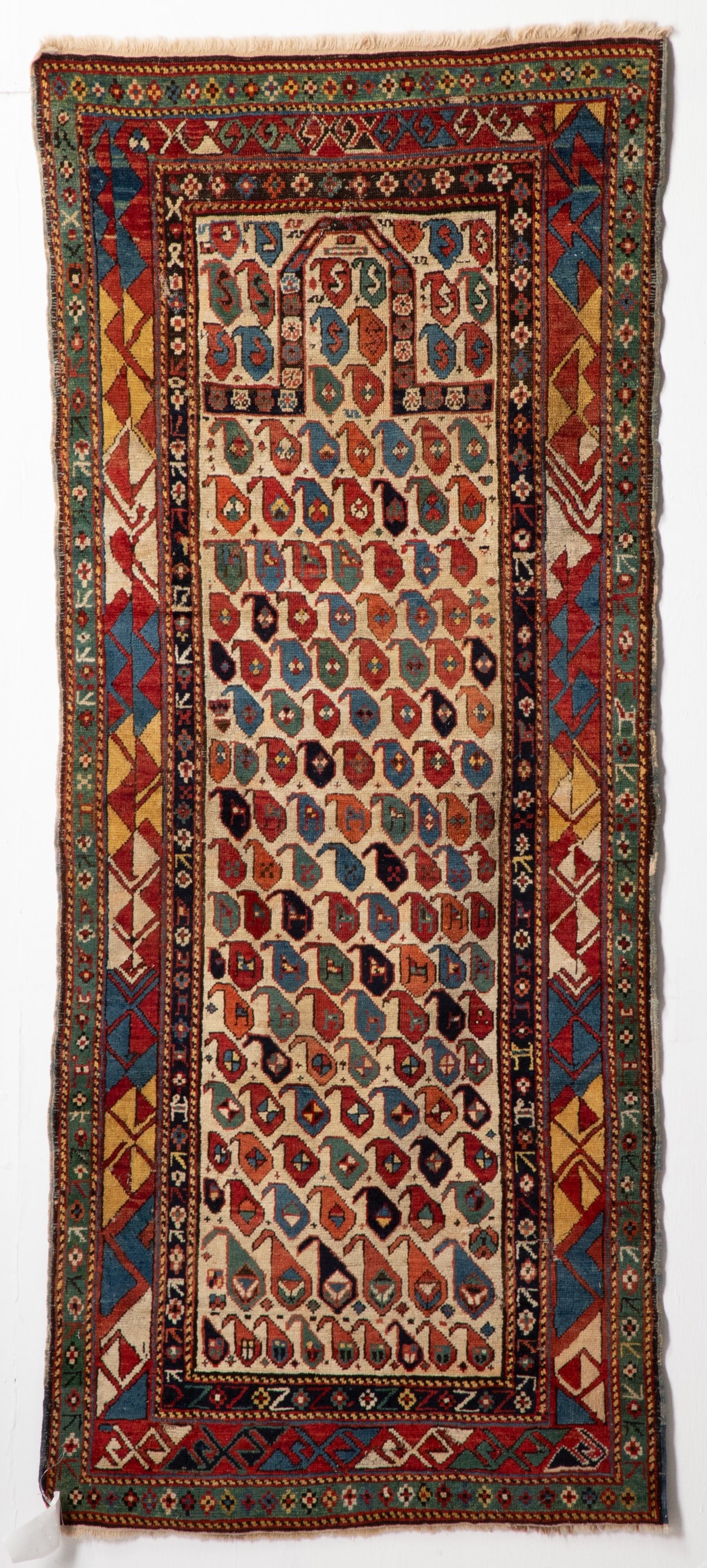 SHIRVAN PRAYER RUG, EAST CAUCASUS, CIRCA 1880. AS FOUND: The ivory mihrab with allover one directional blue and red botehs, below a flattened arch, similar boteh spandrels, within a red border enclosing alternating blue, yellow and ivory diagonal hooked bar