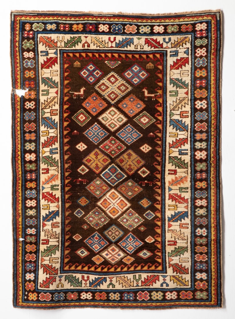 SHIRVAN RUG, EAST CAUCASUS, LATE 19TH CENTURY. AS FOUND: The dark chocolate field with allover polychrome rhombus medallions , supported with combs and ibex, within an ivory calyx border, dark chocolate outer surround enclosing continuous polychrome flower 