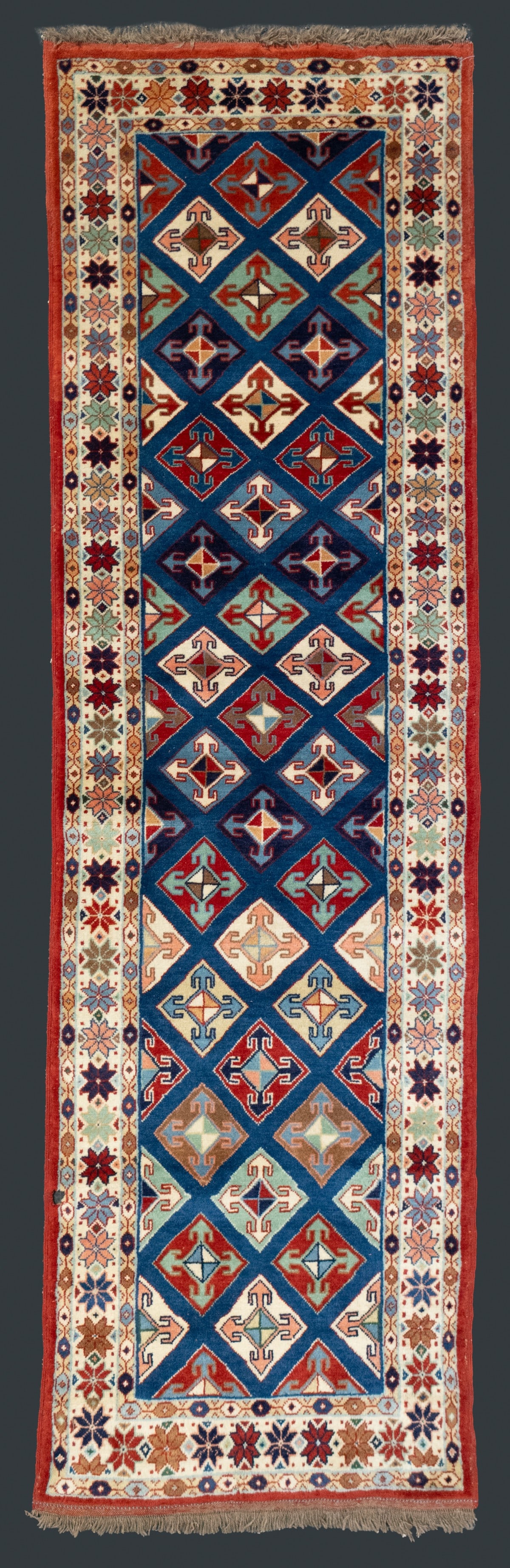 A 20TH CENTURY TURKISH RUNNER, CENTRAL TURKIYE: A nice pile rug with a field of stacked diamond medallions enclosed by an ivory main border filled with polychrome eight-pointed star rosettes. Measures approximately 115 x 33 inches; 9ft.7 inches x 2