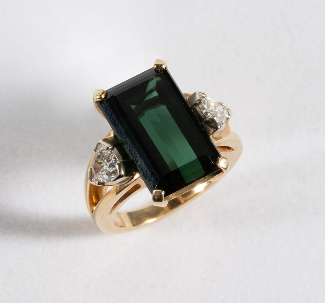 A LADIES 18K GREEN TOURMALINE AND DIAMOND COCKTAIL RING: The fine modern design 18k gold mounting with split shoulders features a near flawless, rectangular, step-cut deep forest green tourmaline flanked by trillion cut diamonds approximately 0.45 carats