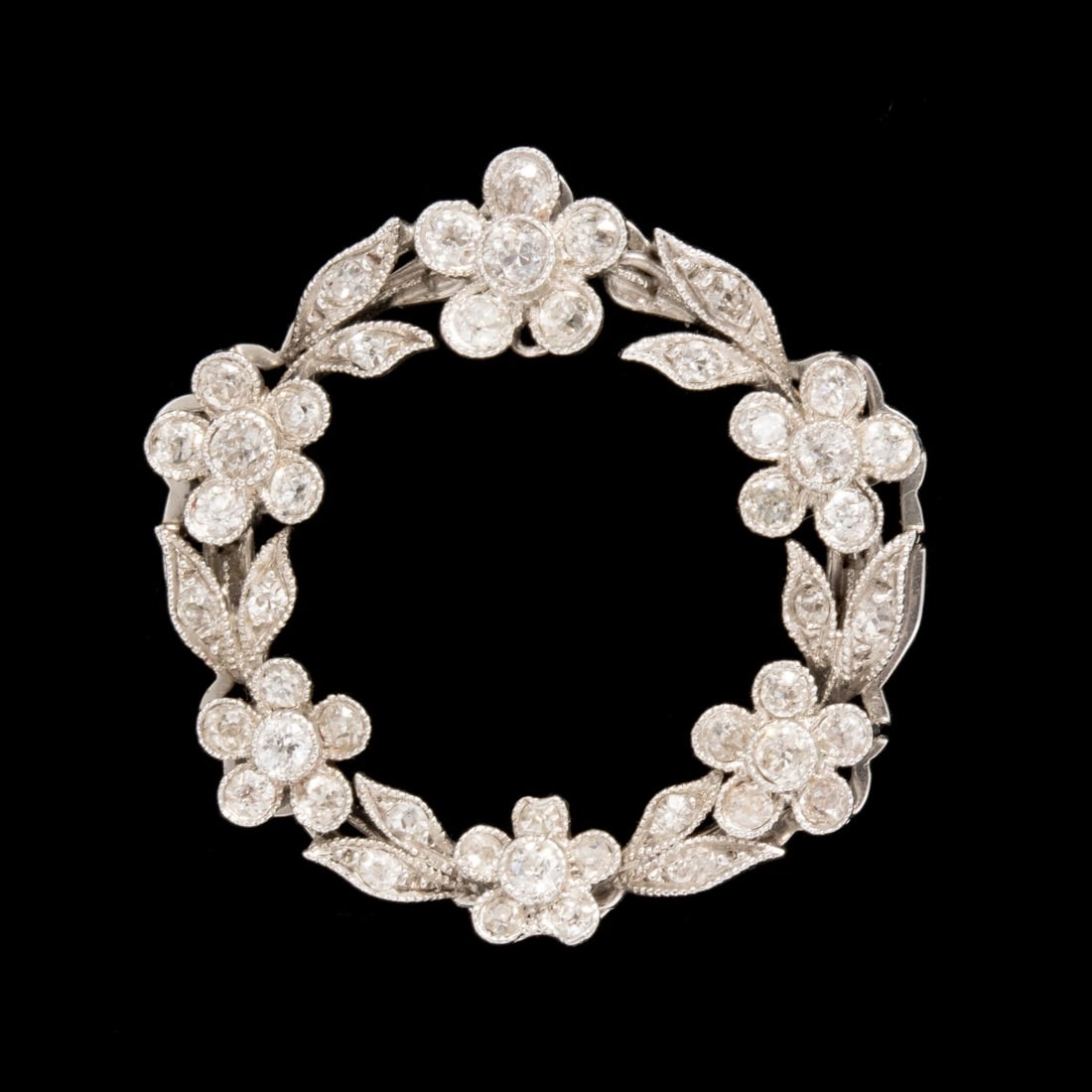 AN EARLY 20C. PLATINUM PIN W/ 48 EUROPEAN CUT DIAMONDS: The platinum pin is designed as a circular garland of flower blossoms and vinery set with old diamonds. Measures 1 x 1 and weighs 6 grams. Without proof of exemption, be aware that internet sales tax