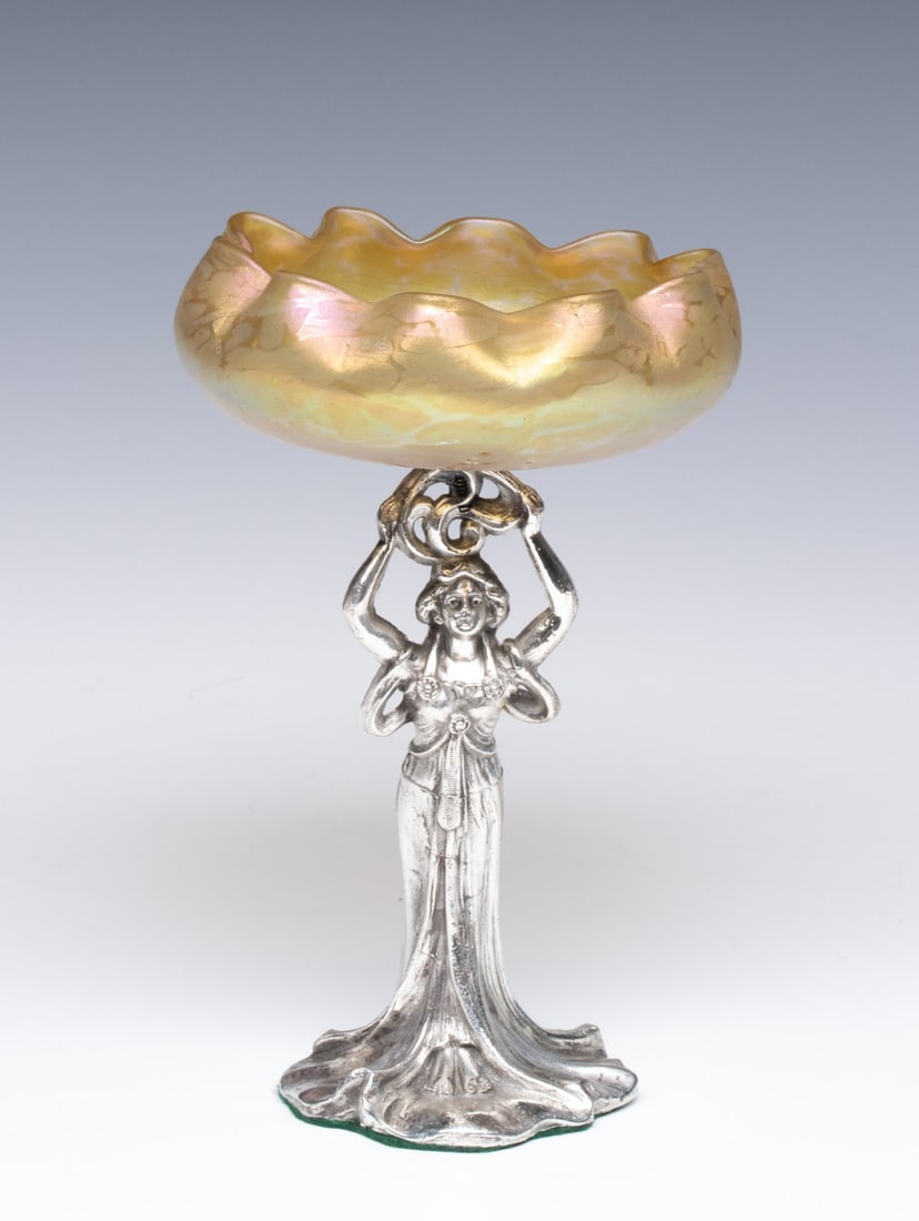 A SILVERED ART NOUVEAU FIGURE WITH AUSTRIAN GLASS: The early 20th century Austrian art glass bowl with iridescent oil spot decoration is raised on an Art Nouveau style figural female standard. Measures 8 x 5 x 5 inches. Without proof of exemption, be