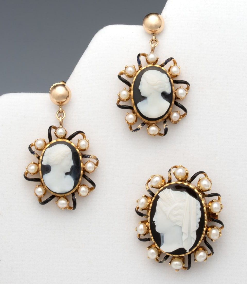 A VICTORIAN GOLD AND HARDSTONE CAMEO SUITE: Each of the three pieces is set with a carved onyx Classical bust cameo in scalloped bezel surrounded by openwork spirals enameled in black and set with pearls. The earrings have been adapted to posts