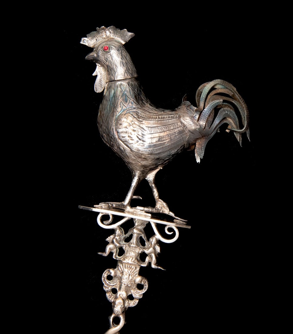 A DUTCH .833 SILVER ARMORIAL SPOON WITH FIGURAL ROOSTER: The armorial presentation spoon with engraved family arms backside of the bowl is topped by an engraved, hollow-bodied rooster having a removable head, thin-cut silver comb and tail feathers and red