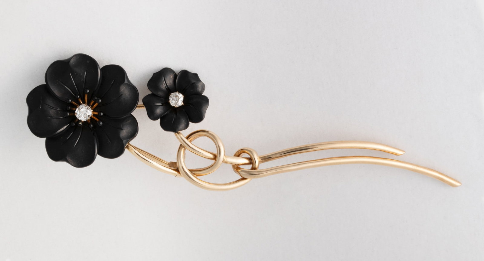 A VICTORIAN 14K GOLD, JET AND DIAMOND MOURNING PIN: The flower-form brooch composed of intertwined gold tendrils set with carved jet flowerheads centered by one larger European cut diamond and one smaller mine cut diamond, the larger accented by a