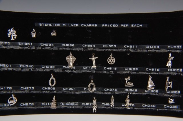 EIGHTEEN STERLING SILVER CHARMS BY BELL: Eighteen sterling silver charms in religious, holiday and Polynesian themes, plus more on their original velvet dealer's show card. Measure from .325 to 1 inches.
