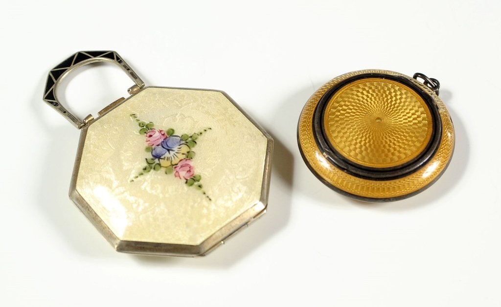 TWO GUILLOCHE ENAMEL COMPACTS: One with art deco influence black enamel bail handle, the other amber color enamel with loss near the hinge. Smaller compact measuring 1.75 inches in diameter, and the larger compact measuring 2.25 x 