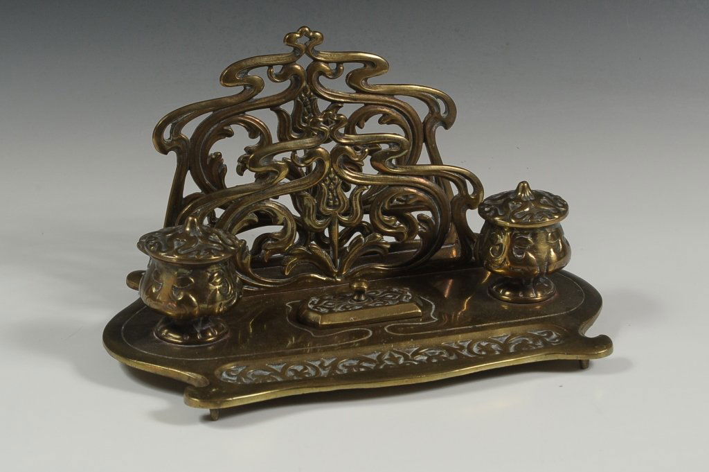 ART NOUVEAU DOUBLE INK WELL DESK STAND: A heavy brass stand with letter holder, two ink wells, stamp box and pen tray. Measures approximately 6.5 x 12 x 8 inches.