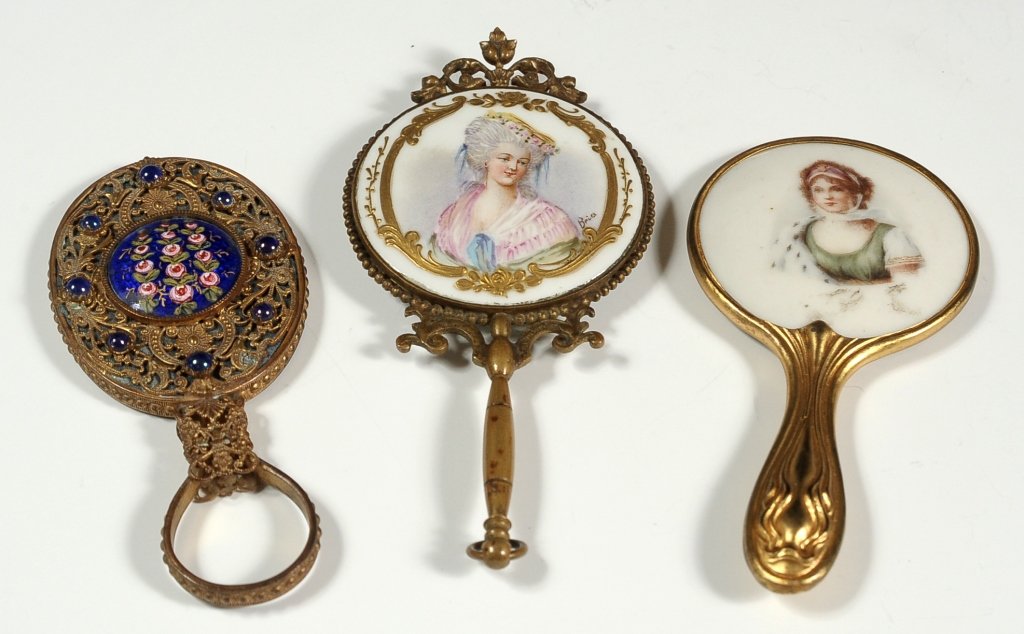 THREE MINIATURE HAND MIRRORS, INCLUDING PORCELAIN AND: Included is a circular hand mirror with hand painted portrait of a woman in pink, artist signed 'Brice,' all in a brass frame with beveled mirror. Plus an oval shape brass filigree mirror with enamel