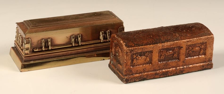 TWO BURIAL CASKET FIGURAL PAPERWEIGHTS: Two pieces with one smaller piece that measures 2 x 4.75 x 1.75 inches, and the larger piece measures 2.25 x 5.75 x 2.25 inches.