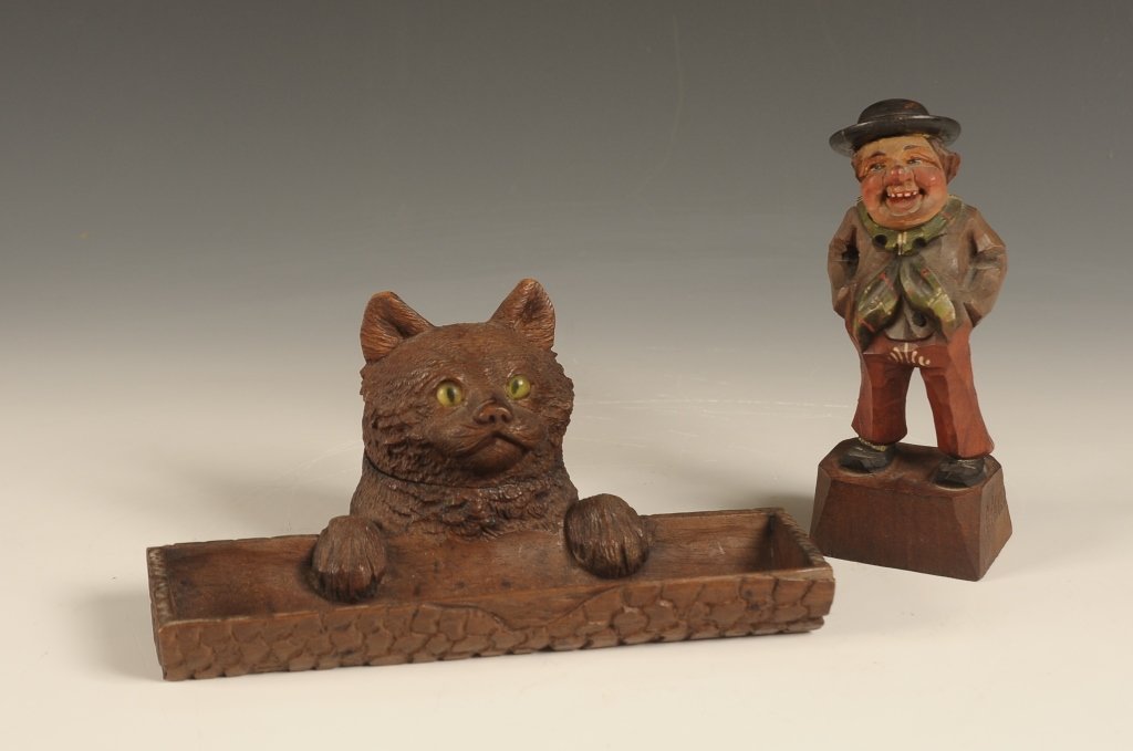 BLACK FOREST CARVED CAT FIGURAL INK WELL: A glass eyed cat with hinged head concealing a glass ink bottle. In front is a tray for pens. Included is a German wood carving. Larger piece measures 4.5 x 7.75 x 4.25 inches and the other figural pi