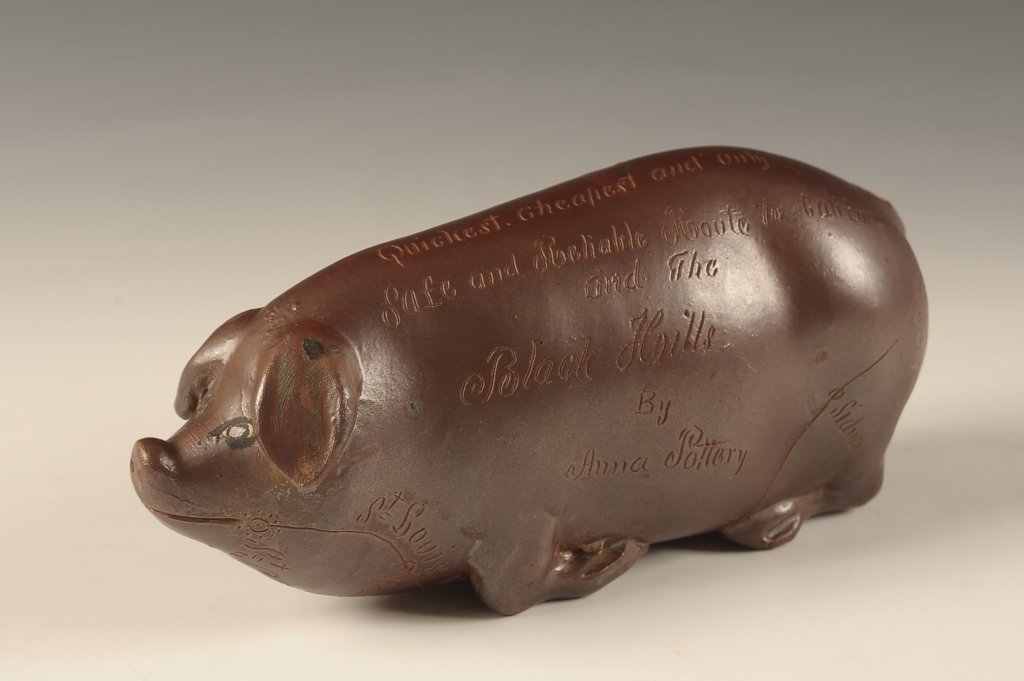 ANNA POTTERY 'BLACK HILLS' RAILROAD FLASK: A pig form stoneware flask with incised decoration and lettering that reads, "Shortest, quickest, cheapest, and only safe reliable route to California and the Black Hills for the St. Louis, Kansas Cit