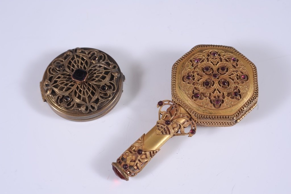 FILIGREE COMPACT AS A HAND MIRROR, PLUS ANOTHER: Goldtone filigree duo compact with jewels, stylized as a hand mirror, lipstick in the handle, hinged mirror over a rouge well with a quilted puff, powder well with a rotary sifter and puff, unmarked,