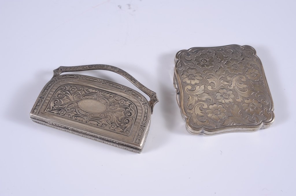 EMBOSSED SILVERTONE COMPACT AND VANITY CASE: Silvertone compact embossed with florals, framed beveled mirror in the lid, mesh sifter in the base, unmarked, measures 2.25 x 2.75 inches. Plus a silvertone purse-shaped vanity case with a rigid hand