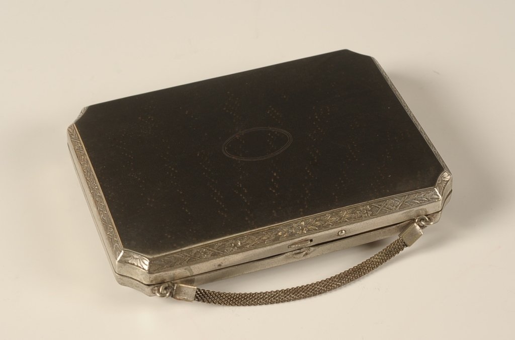EAM VANITY CASE: Silvertone vanity case with a framed mirror in the lid, mesh chain handle, base holds a lidded rouge pan, two lipsticks and two hinged powder wells, marked on the inside base, measures 3 x 4.5 inches.