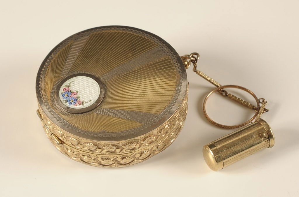 D.F.BRIGGS CO. COMPACT WITH FINGER RING & LIPSTICK: Two tone duo compact with guilloche medallion on top, chain with finger ring and lipstick fob, hinged mirror over a rouge well in the lid, base holds a powder well with partial pan, marked in the base