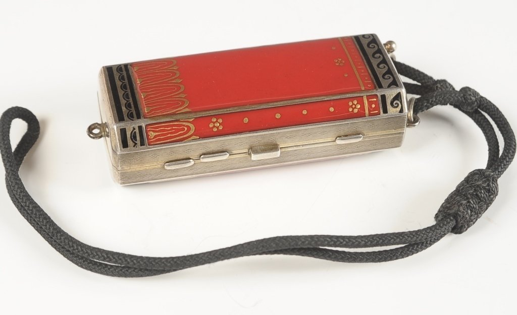 RED & BLACK CHAMPLEVE ENAMEL BOLSTER MINIAUDIERE: Red and black champlevÃ© enamel bolster miniaudiÃ¨re with cord handle, mechanical pencil inserts in the top, hinged compartment on one side with framed mirror, other side holds a hinged rouge and