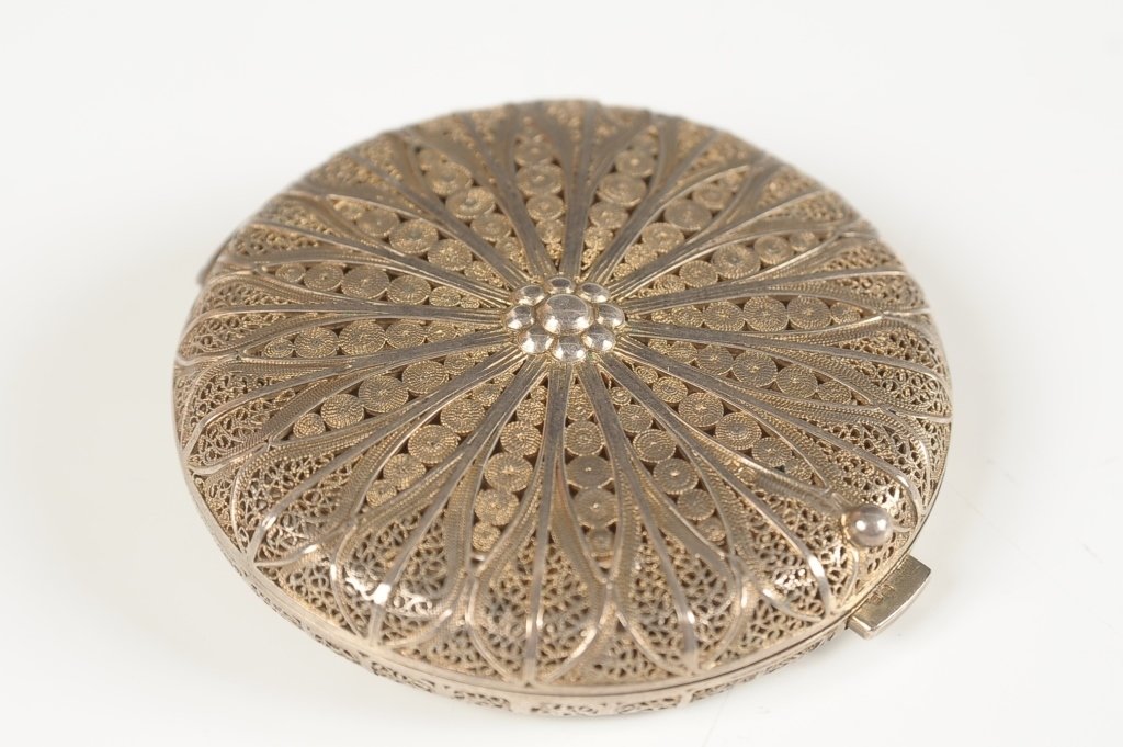 SILVER FILIGREE COMPACT: With a framed beveled mirror in the lid, metal and mesh sifter with puff in the base, faint hallmarks on the frame of the sifter, measures 2.5 inches.