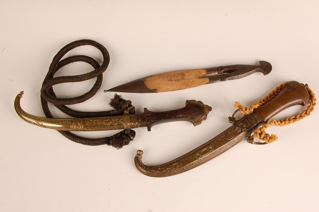 TWO MOROCCAN DAGGERS AND A TUNISIAN DAGGER: Lot includes two Moroccan Koumiyyah daggers and scabbards, and a Tunisian 'fork' dagger. Koumiyyahs include wooden grips, one with etched brass overlaid pommel - but missing throat trim. Other with si