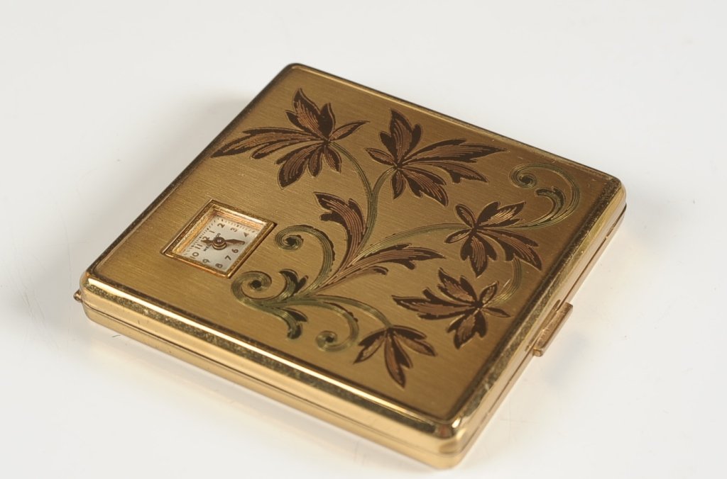 AMERICAN BEAUTY DUO COMPACT WITH WATCH: Goldtone compact with a peek through watch in the lid, framed mirror in the lid, watch, hinged rouge well and hinged powder well in the base with a puff, marked on the powder well lid, measures 2.75 i