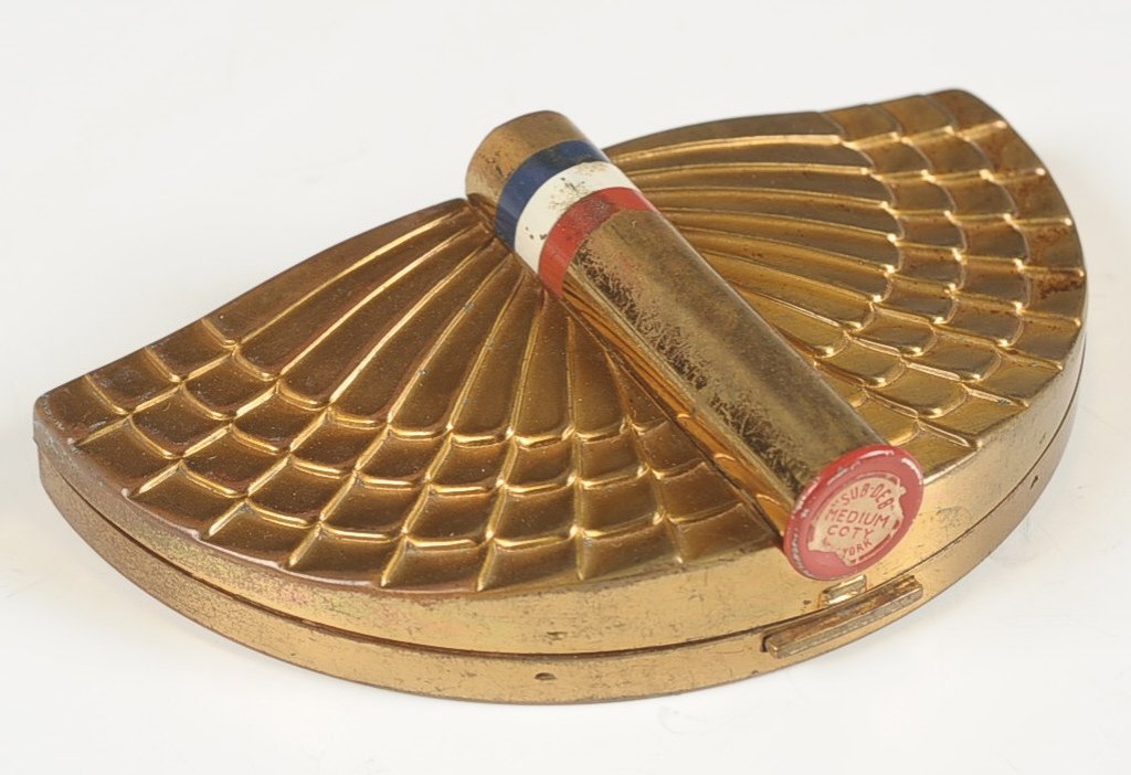 1939 COTY 'FLYING COLORS' DUO COMPACT: Half-moon wing design with red, white and blue banded lipstick, framed mirror in the lid, rouge well with pan in base, hinged powder well, marked on the bottom, measures 2.25 x 4 inches.