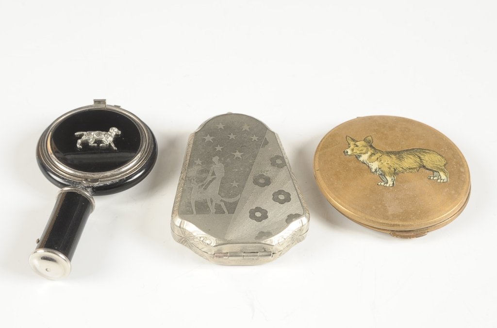 THREE VINTAGE COMPACT WITH DOG THEMES: Black enamel duo compact designed as a hand mirror with a jeweled dog on top, lipstick in the handle, metal mirror over a rouge well in the lid, puff and rotary sifter in the base, measures 3.5 inches