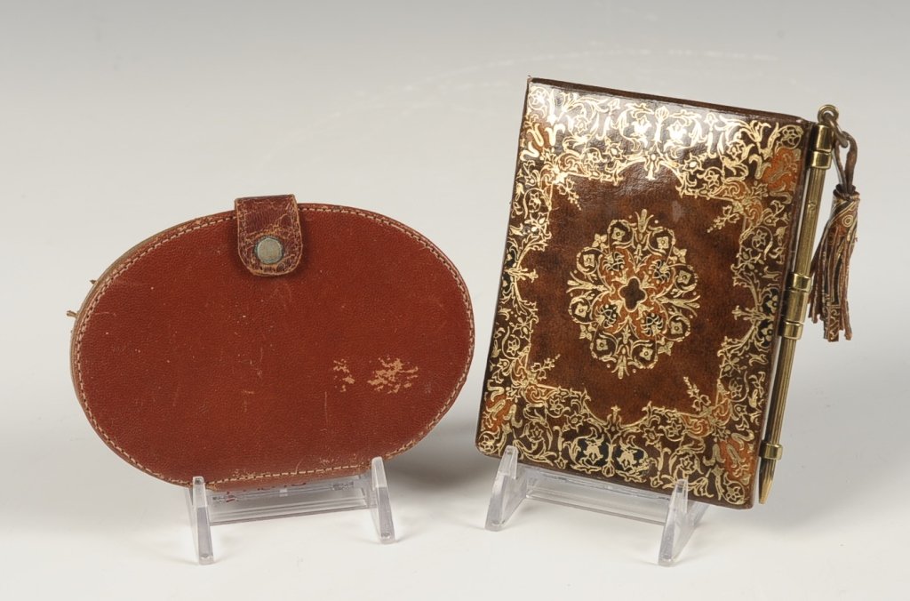 GILDED LEATHER BOOK-STYLE COMPACT, PLUS ANOTHER: Gilded and embossed leather compact made in the style of a book with a faux pencil closure and leather tassel, mirrored lid, mesh sifter in the base, unmarked, measures 4 x 3.25 inches, very good. Plu