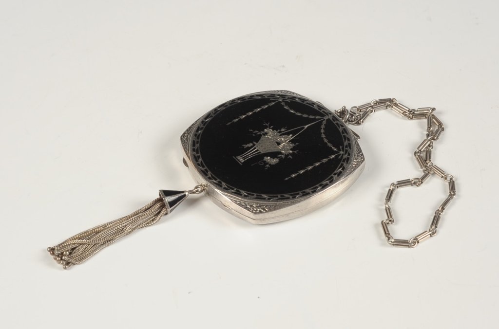 STERLING COMPACT WITH BLACK ENAMEL: Chain handle and metal tassel, framed mirror in the lid, base holds a partial rouge/powder pan combo with one half-round puff, marked on the inside base, measures 2.75 x 2.5 inches, weighs 3.3 ozt.