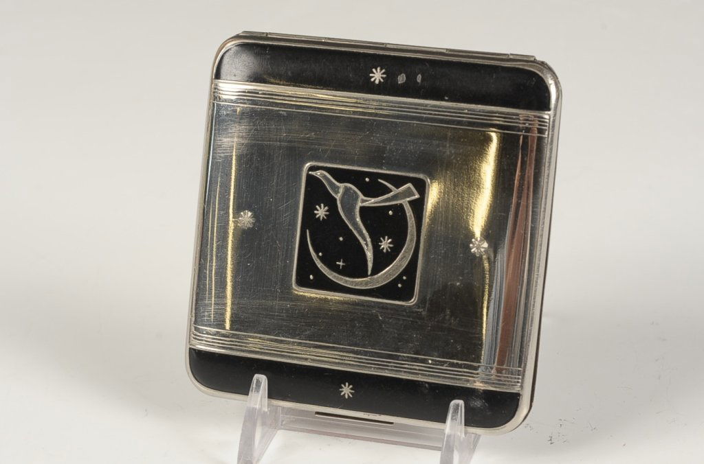HUDNUT 'LE SOIREE' VANITY CASE: Black enamel on embossed silvertone large vanity case with a moon and bird design on top, framed mirror in the lid, base holds two hinged wells plus a rouge well with pan, no puffs present, marked on