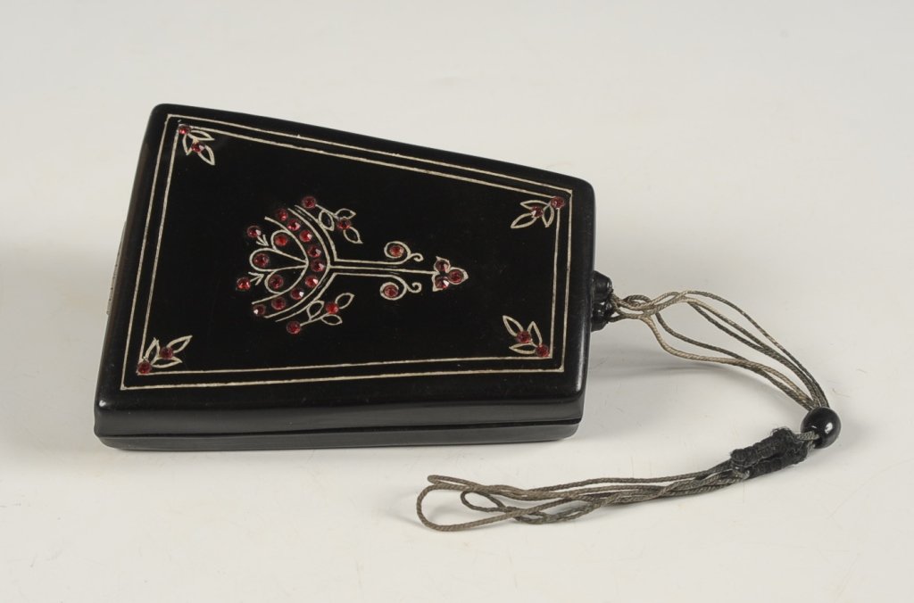 JEWELED PLASTIC VANITY CASE: With a cord and bead closure, mirrored lid with a pocket for a comb (no comb present), base holds wells for powder, rouge an lipstick, unmarked, measures 3.75 x 3 inches.