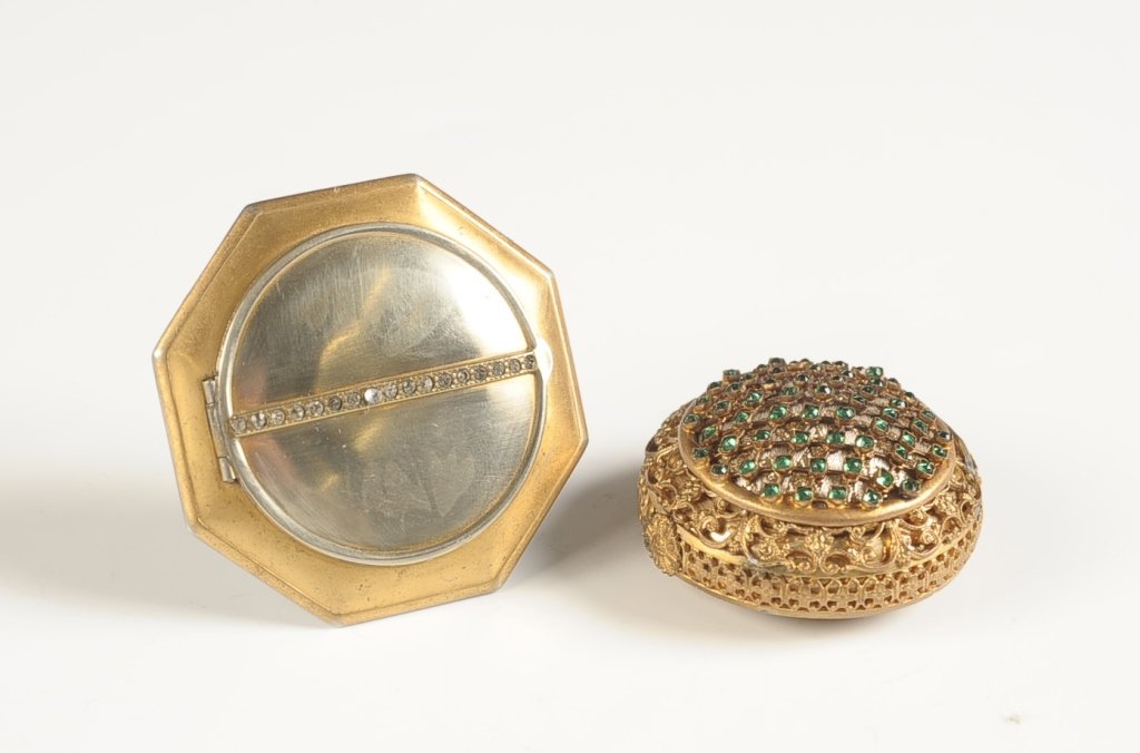 JEWELED FILIGREE COMPACT & JEWELED LA MODE COMPACT: Goldtone filigree compact with green jewels on top, framed mirror in the lid, puff present, unmarked, measures 1 inch. Plus a La Mode duo compact with jewels on top, hinged metal mirror over a rouge w