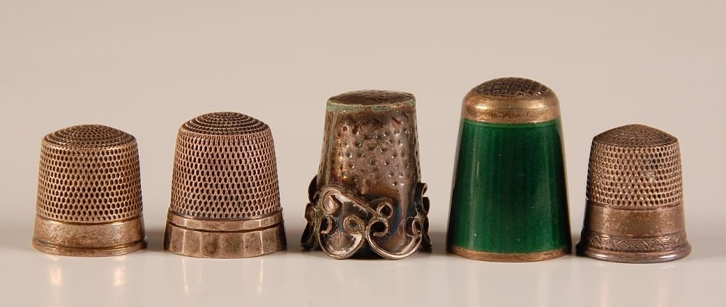 FIVE ANTIQUE STERLING SILVER SEWING THIMBLES: Including one with green enameling. Group ranging in size from .75 inches in height, down to .5 inches in height